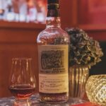 A premium bottle of Craigellachie 21-year-old Speyside single malt scotch whisky, a top pick for high-value whisky investment, sits elegantly on a table with a glass of whiskey and an ornamental plant.