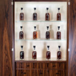 A display cabinet with three shelves presents a curated selection of twelve high-value whisky bottles, featuring a coveted Dalmore Cask, all elegantly arranged within a sturdy wooden frame. This exquisite collection is ideal for the discerning whisky investor seeking both beauty and investment opportunity in one refined asset.
