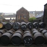 Rows of premium whisky barrels are stacked in an outdoor courtyard, framed by historic stone buildings, showcasing the blend of tradition and investment potential.