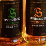 On a wooden surface, two bottles of premium Springbank single malt scotch whisky are displayed, showcasing their value with labels indicating 15-year-old and 10-year-old varieties, perfect for investment portfolios.