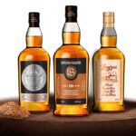 Resting on a wooden barrel, three premium Scotch whisky bottles—Hazelburn, Springbank Cask Whisky Investment, and Longrow—exemplify the enticing allure of golden liquid investments for collectors and connoisseurs alike.