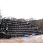 Stacks of premium whisky barrels are arranged in a triangular formation outdoors, framed by bare trees and sand, showcasing the essence of high-value brand investment.