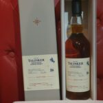 A premium Talisker 26-year-old single malt Scotch whisky bottle sits elegantly in its box on a plush red upholstered seat, offering a tempting opportunity for discerning investors and whisky enthusiasts seeking high-value additions to their collections.