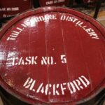 A high-value whisky investment image showcasing a wooden barrel lid, featuring "Tullibardine Distillery, Cask No. 5, Blackford" elegantly stenciled in white on its rich red surface.