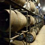 In a dimly lit, climate-controlled storage area, premium whisky barrels are artfully stacked on metal racks, showcasing the meticulous aging process that enhances their investment value.