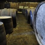 In a dimly lit cellar, premium wooden barrels of high-value whisky investment line the rustic dirt floor.