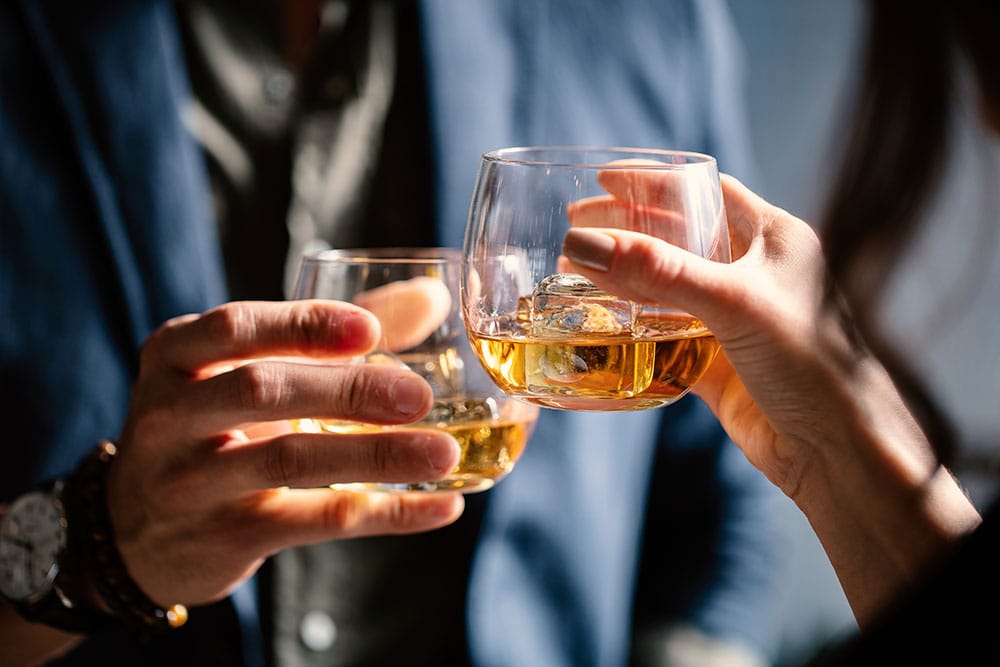 two people clinking whisky glasses in toast