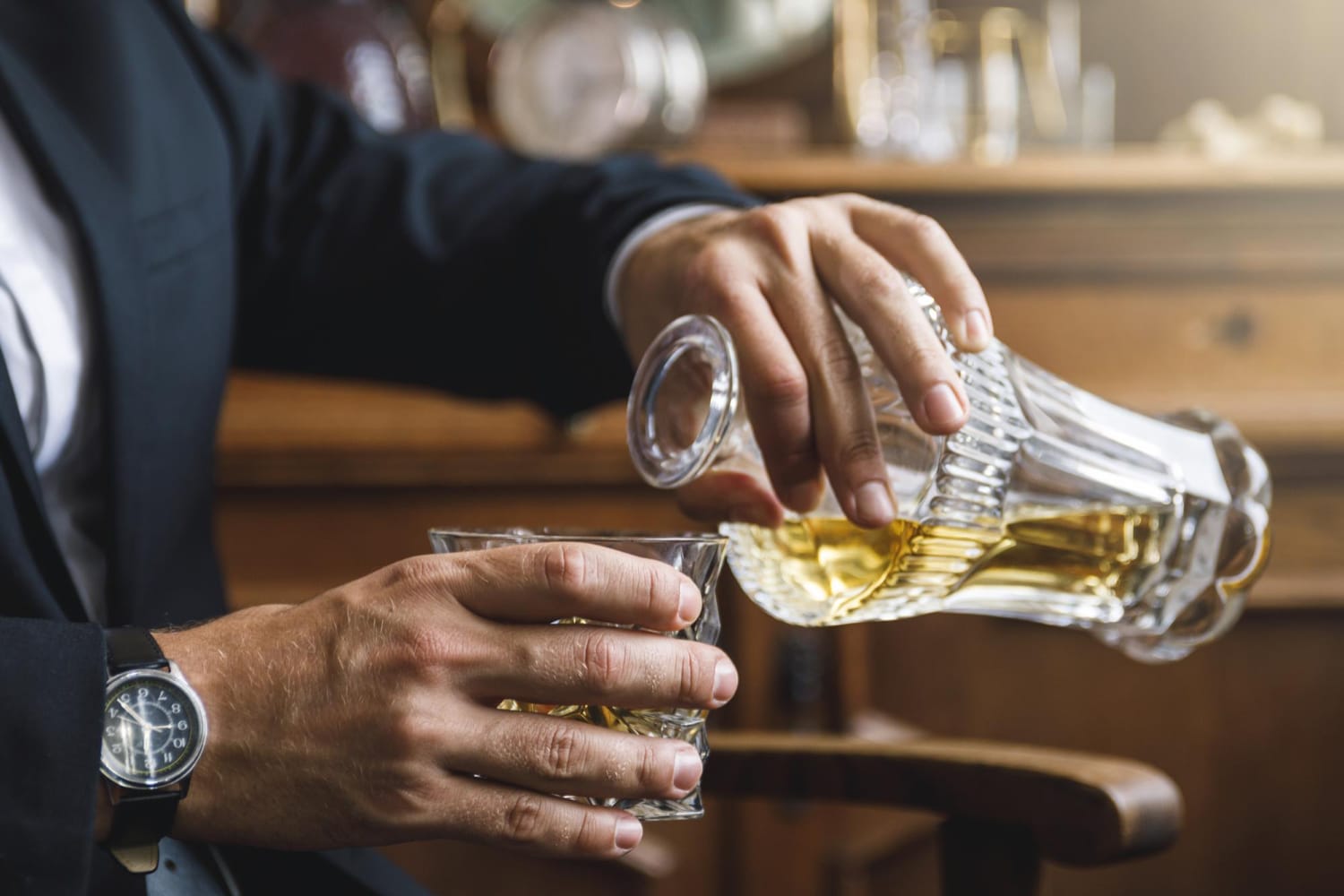 smart investors: A well-dressed investor in a suit pours premium whisky from a crystal decanter into a glass, seated in an elegant wooden chair—capturing the sophistication and luxury of whisky investing.