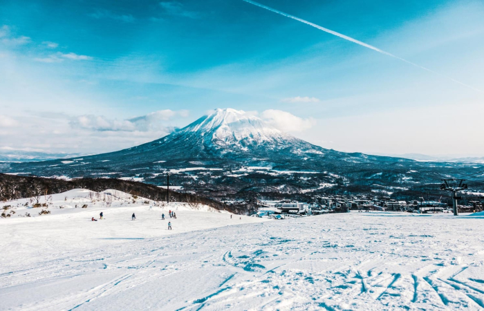 Scenic mountain ski slope with skiers, snowy peaks, and crisp blue sky, evoking premium whisky and refined investment ambiance.