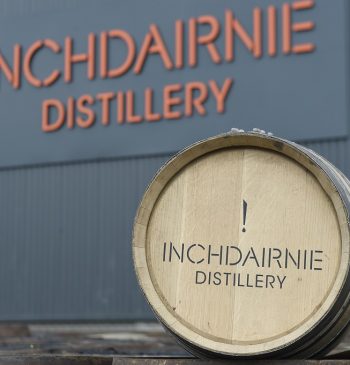 A wooden barrel, emblazoned with "InchDairnie Distillery," stands proudly against the distillery's own building, symbolizing high-value whisky investments and showcasing the brand's dedication to premium craftsmanship and long-term growth.