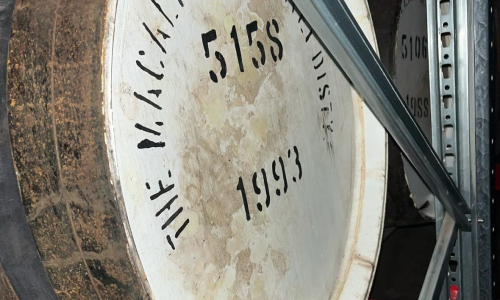 A close-up of a premium whisky barrel labeled "The Macallan Glenlivet Distillery 5158 1993," resting on a rack, ideal for investors.