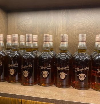 Rare, aged whisky bottles, such as the prestigious Glenfarclas 60-year-old, are elegantly displayed on a wooden shelf, reflecting their high investment value and premium quality.